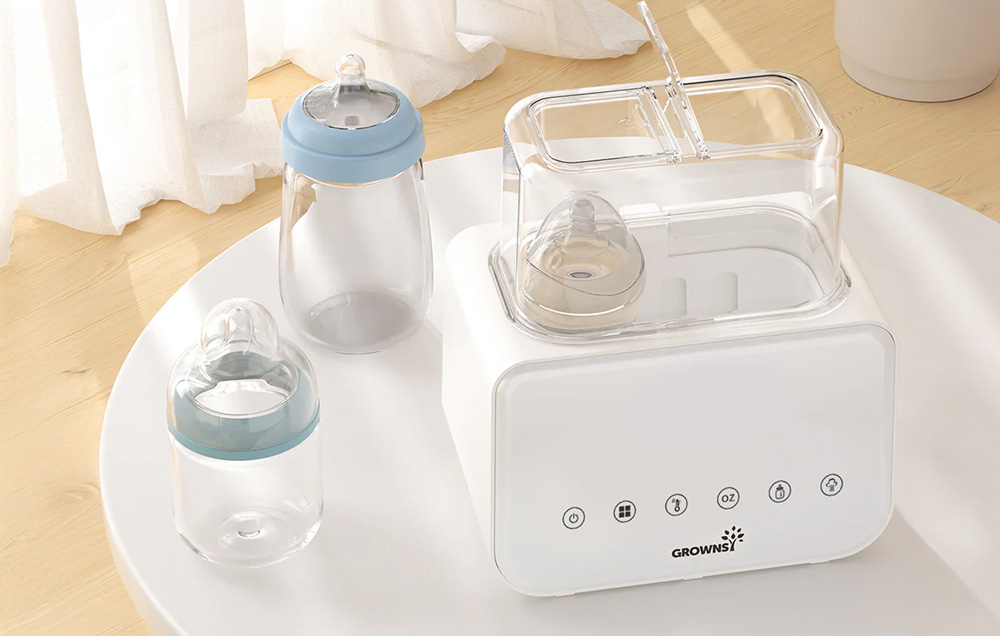 A bottle warmer with the lid open, surrounded by empty bottles on a table