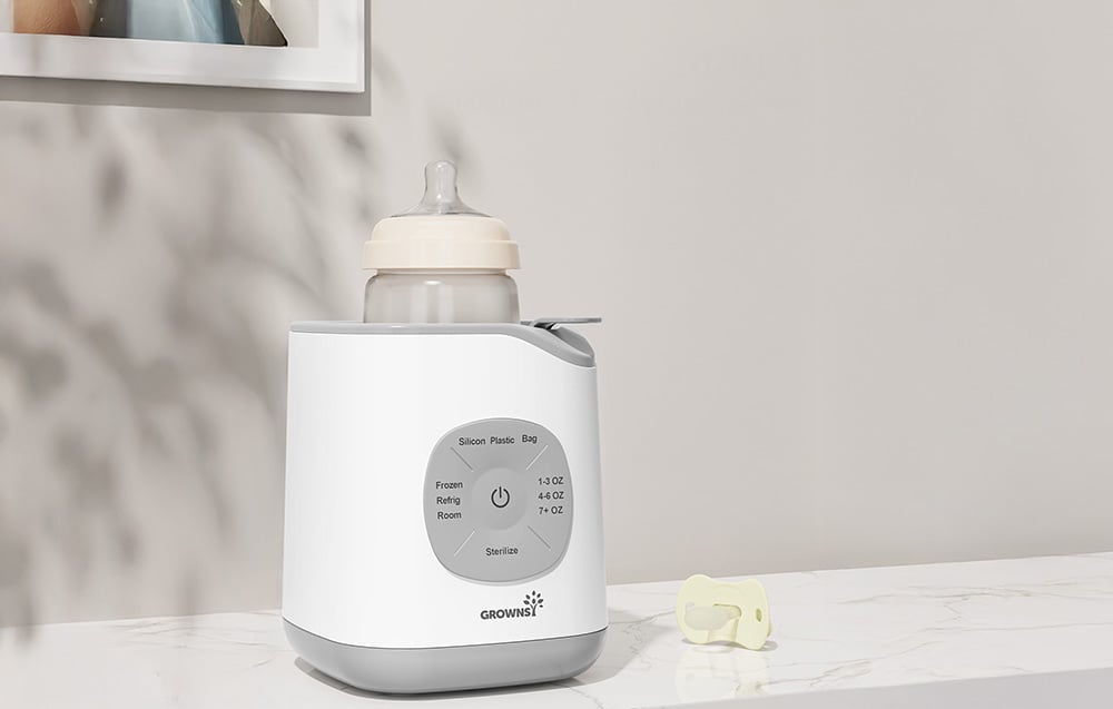 Bottle warmer with one bottle and a nipple lying next to it on a marble countertop