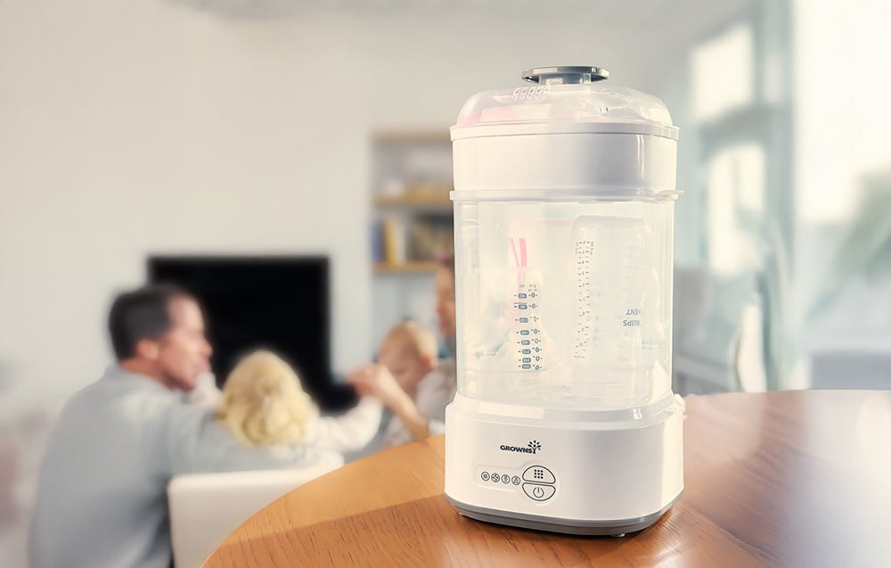 Sterilizer with a set of bottles in a bright interior, with a family with children in the background