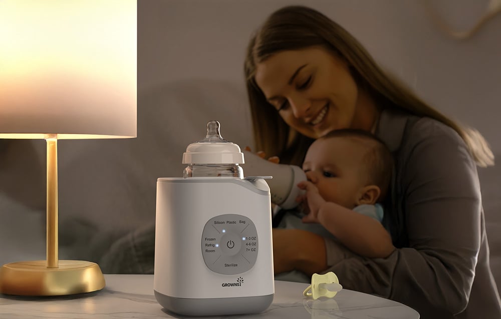 A woman is feeding her baby in the background, and on the table next to the lamp there is a bottle warmer with a bottle inside