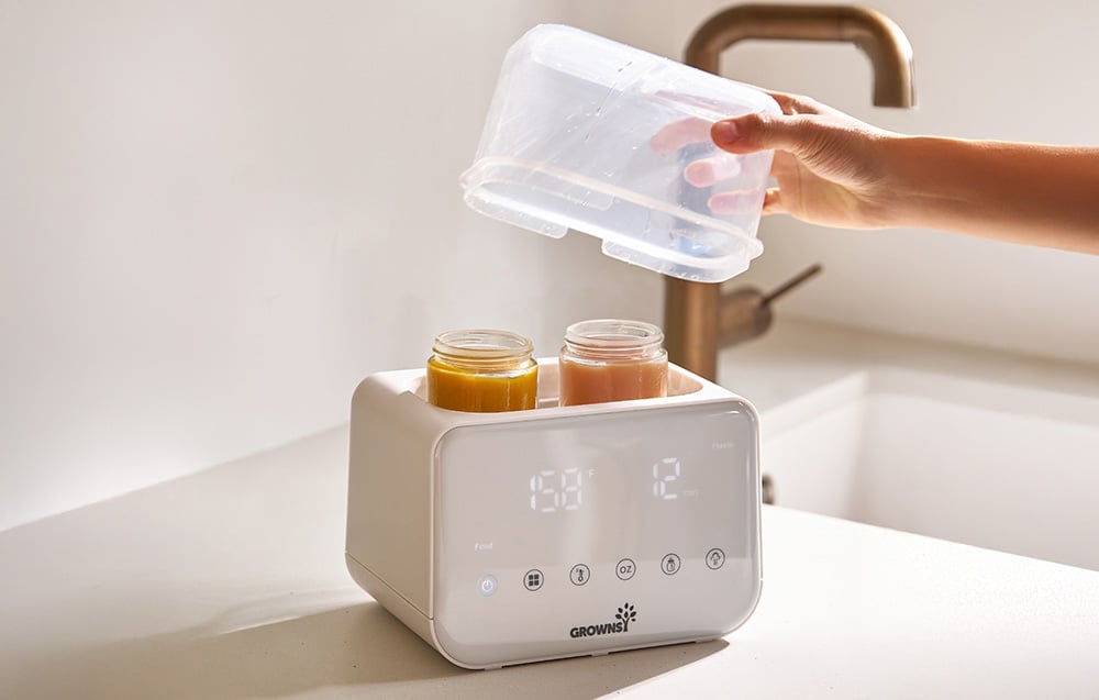 A person removes the lid from the warmer, in which two jars of food are being heated