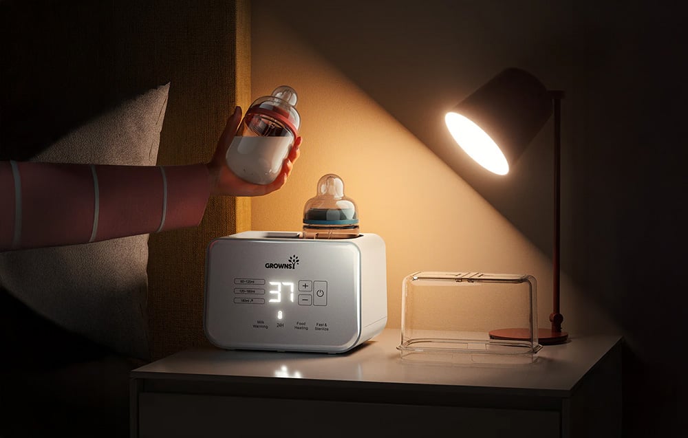 Bottle warmer on a bedside table, one bottle held in the hand, the other on the device